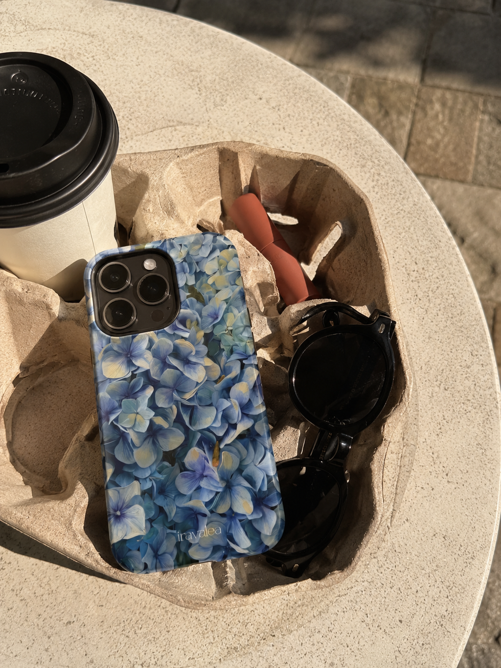 Phone case with blue floral pattern on a stone surface with a coffee cup and sunglasses.